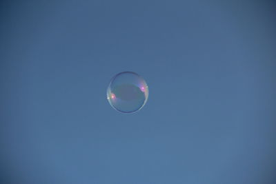 Low angle view of bubbles against clear blue sky