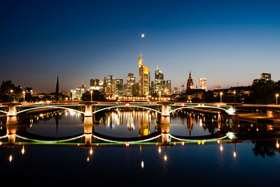 Illuminated bridge over river with buildings in background at night in frankfurt, germany 