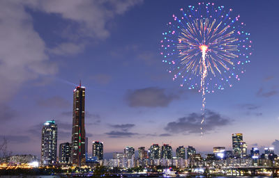 Firework display over illuminated buildings in city against sky at night