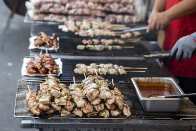 Midsection of vendors cooking meat on barbecue grill