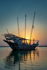 Sailboats moored on sea against sky during sunset