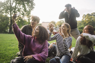 Happy teenage girl taking selfie with male and female friends through smart phone at park