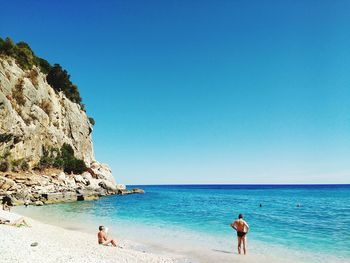 People at beach against clear blue sky