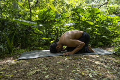 Young latin man arranging his yoga mat, inside a forest on a plain, direct contact with nature