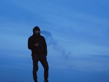 Full length of man smoking pipe cigarette while standing against blue sky