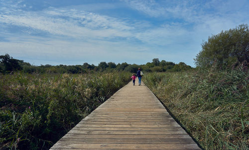 Rear view of woman with daughter walking on boardwalk amidst plants