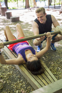 Man helping woman in lifting wooden weight at outdoor gym