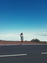 Rear view of man on road against blue sky