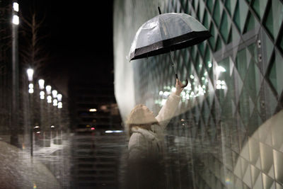 Digital composite image of woman holding umbrella standing by building in city