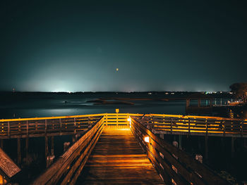 Illuminated pier over sea against sky at night