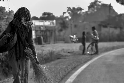 People standing on road by field against sky