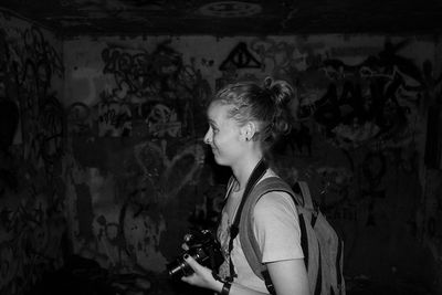 Side view of woman with camera by graffiti wall in abandoned room