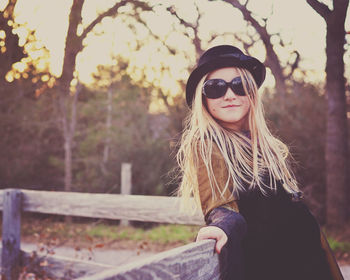 Beautiful smiling woman wearing sunglasses by fence against trees