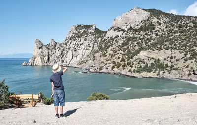 A boy in casual clothes standing on the shore of the bay and looking at the rocks. travel concept.