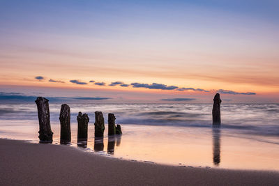 Silhouette wooden posts on beach against sky during sunset