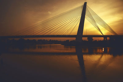 Silhouette bridge over river against sky during sunset