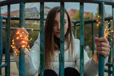 Portrait of young woman holding illuminated lighting equipment while crouching in play equipment