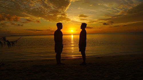 Silhouette people standing on beach during sunset