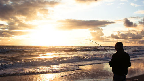 Silhouette man fishing on shore during sunset