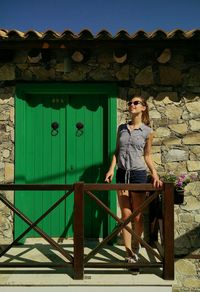 Full length of young woman standing in balcony on sunny day