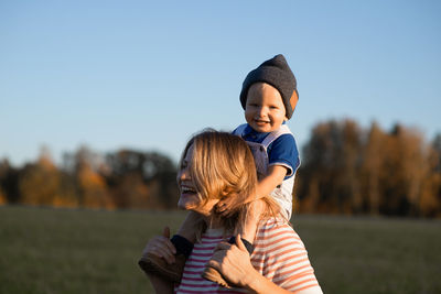 Happy mother carrying son on shoulders while standing in park