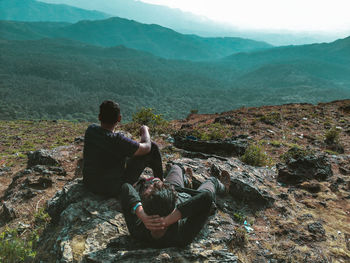 Rear view of men sitting on rock looking at mountains