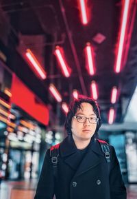 Portrait of young asian man standing against colorful neon lights and architecture.