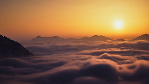 Scenic view of dramatic sky over silhouette mountains during sunset