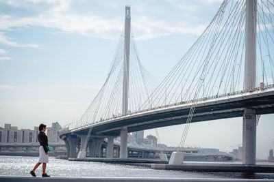 Woman standing in city by river against bridge