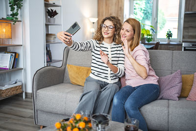Portrait of young woman using mobile phone while sitting on sofa at home