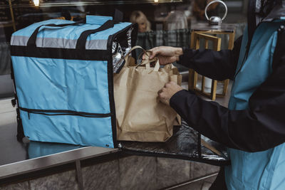 Midsection of delivery man putting package order in backpack outside deli store