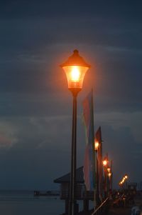 Illuminated street light by sea against sky at sunset