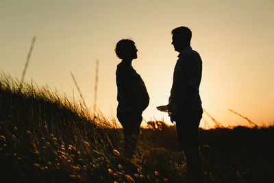 Silhouette people standing on field against sky during sunset