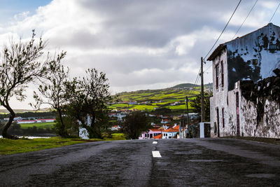 Road amidst trees and buildings against sky