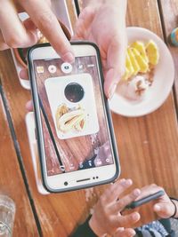 Cropped image of woman photographing food on table at restaurant