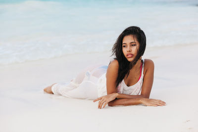 Young woman lying on sand at beach against sky
