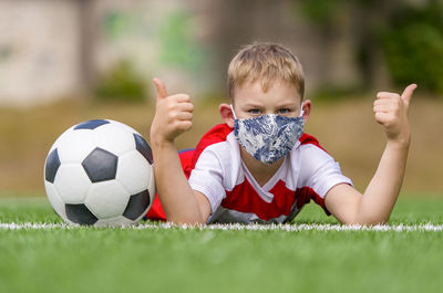 Portrait of boy lying on grass with soccer ball