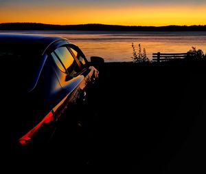 Silhouette car on shore against sky during sunset