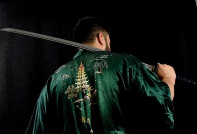Rear view of man holding sword against black background