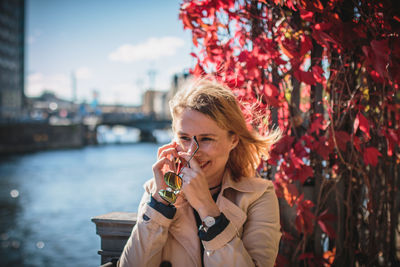 Young woman using phone while leaning on railing by creeper plant