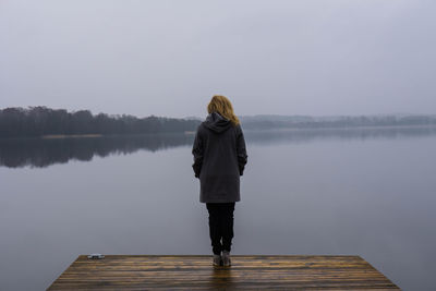 Rear view of woman walking on pier in front of lake against clear sky