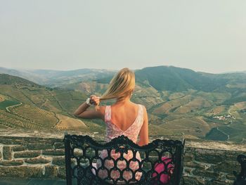 Rear view of woman sitting on chair at observation point against landscape