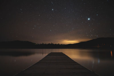 Pier over lake against sky at night