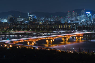 Illuminated bridge over river in city at night