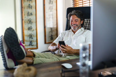 Smiling male professional using mobile phone while relaxing on chair at home office