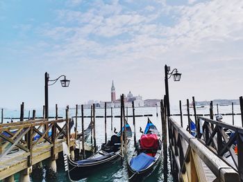 Gondolas moored in canal against sky