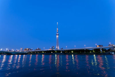 Illuminated tokyo sky tree with reflection in sea against blue sky at night