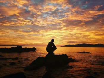 Silhouette man on rock by sea against sky during sunset