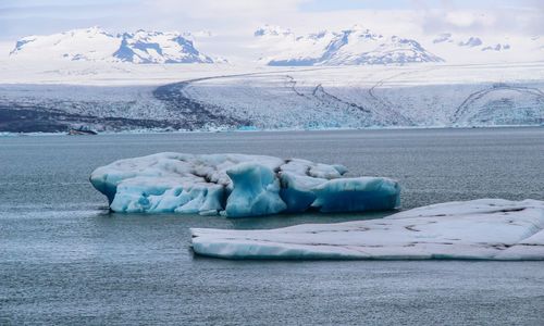 Ice floating on lake against snowcapped mountains