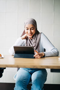 Content muslim female in hijab and talking on video chat via tablet while sitting at table in cafe